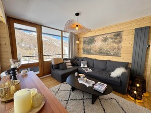 A modern living room with a sofa, coffee table, and a large window offering a mountain view. - Spacious apartment - 6 guests (Vars)