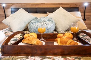 A bed with a wooden headboard, two pillows, a decorative cushion, a tray with croissants, oranges, and glasses of orange juice. - Villa Camila - El Pajar (Villarraba)