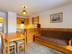 Een kleine keuken met houten kastjes, een eettafel met stoelen en een bank.