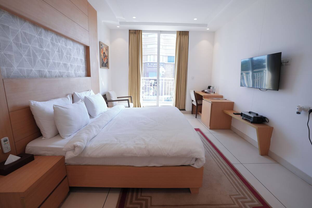 A modern hotel room with a large bed, a desk, a television, and a view of the outside.