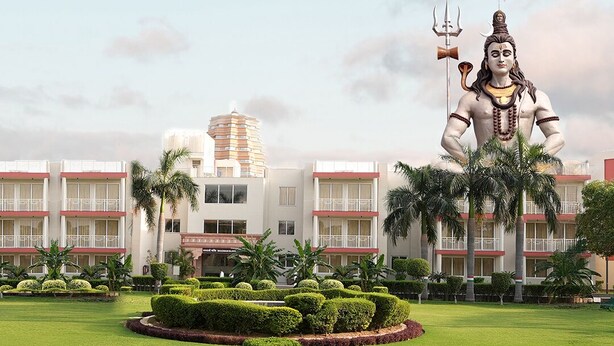 Una gran estatua de una deidad en una zona ajardinada, con un edificio de hotel al fondo.