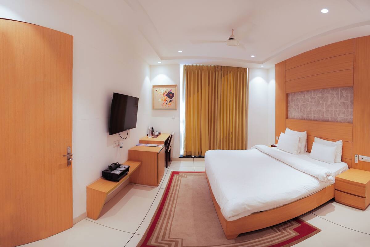 A hotel room with a bed, bedside tables, a TV, a desk, and a chair.