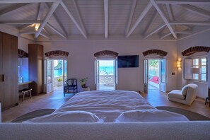 A bedroom with a large bed, a desk, a chair, and a view of the ocean through an open door. - 1-bedroom apartment in the heart of Parga (Parga)