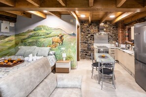 A cozy room with a bed, a dining table, and a kitchen area with a stone wall and wooden beams. - Villa Camila - La Cuesta (Villarraba)