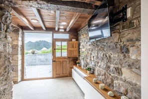 Un interior rústico de piedra con una puerta de madera, un televisor de pantalla plana montado en la pared y un estante pequeño con objetos decorativos.