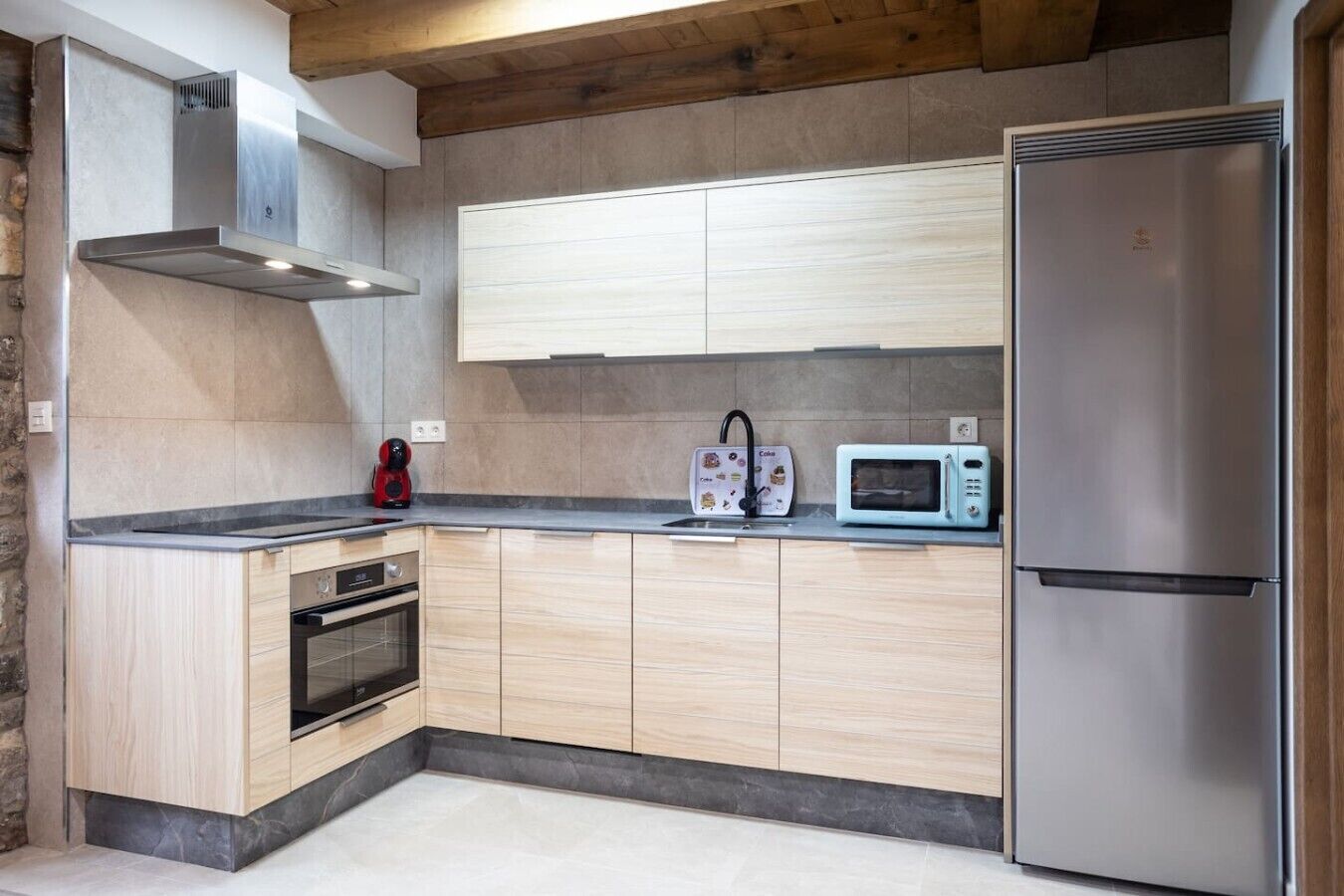 A modern kitchen with light wood cabinets, a stainless steel refrigerator, a microwave, and a built-in oven.