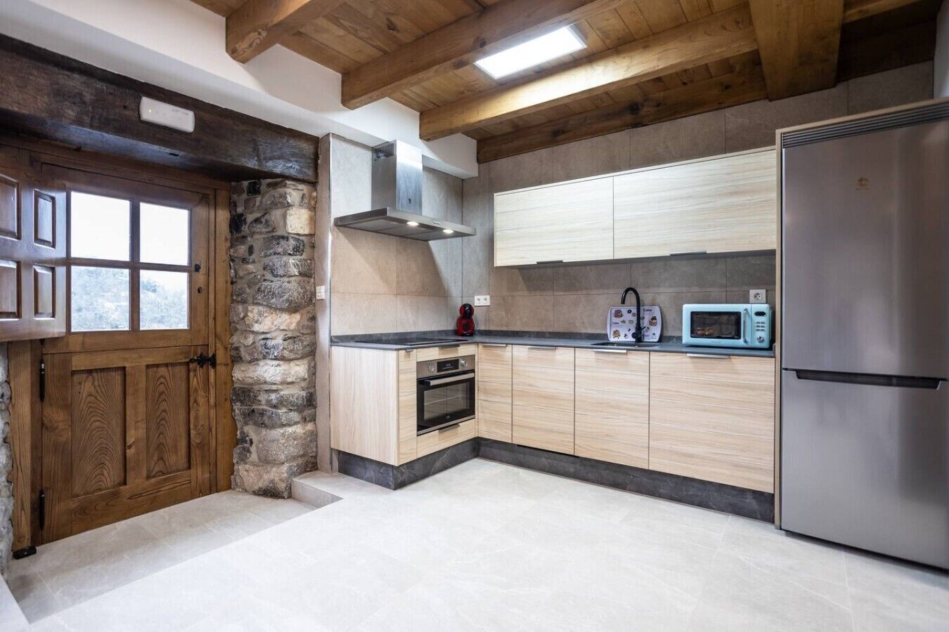 Une cuisine avec un mur en pierre, des armoires en bois, un réfrigérateur en acier inoxydable et un four à micro-ondes.