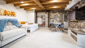 A cozy living area with a sofa, a dining table with chairs, a kitchen area with a stone wall, and a ceiling with wooden beams. - Villa Camila - El llagar (Villarraba)