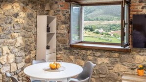 A stone-walled room with a round table, chairs, a white cabinet, and a window overlooking a landscape. - Villa Camila - El llagar (Villarraba)