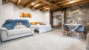 A cozy room with a sofa, a bed, a dining table with chairs, and a stone wall. - Villa Camila - El llagar (Villarraba)