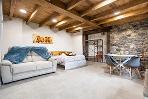 Una habitación acogedora con sofá, cama, mesa de comedor y sillas, y una pared de piedra.