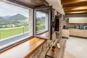 A kitchen with a stone countertop, a window with a view of a green landscape, and wooden cabinets. - Villa Camila - El llagar (Villarraba)