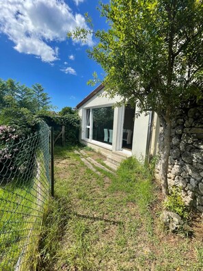 Une maison avec un mur en pierre, une cour gazonnée et une clôture en treillis métallique.