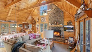 L’intérieur chaleureux d’un chalet avec une cheminée en pierre, des poutres en bois au plafond et un coin repas comprenant une table et des chaises.