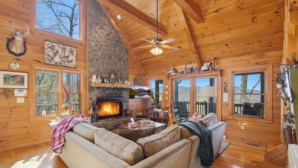 L’intérieur d’un chalet chaleureux, avec une cheminée, des murs en bois et un ventilateur de plafond.