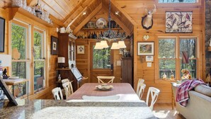 L’intérieur d’un chalet en bois comprend une table à manger, des chaises, un lustre et une tête de cerf accrochée au mur.