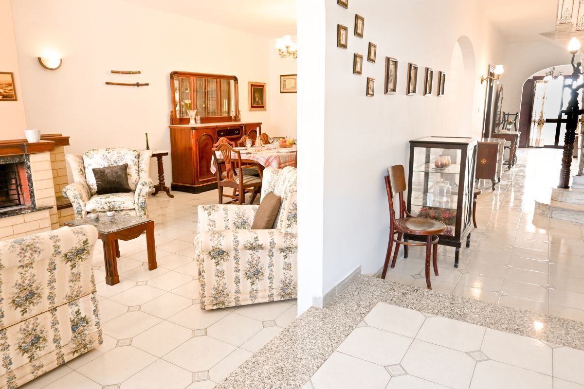A spacious living room with floral-patterned sofas, a wooden coffee table, and a dining area with a wooden cabinet and table.