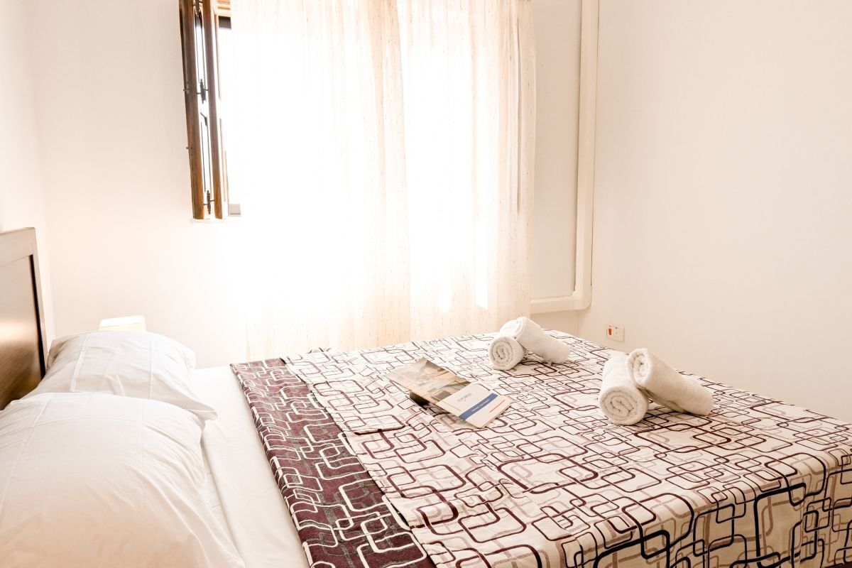 A hotel room with a bed, a window with curtains, and a towel on the bed.