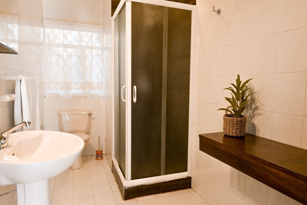Un baño con lavamanos blanco, inodoro y cabina de ducha con paredes de vidrio.
