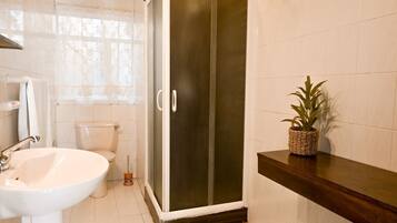 Un baño con lavamanos blanco, inodoro y cabina de ducha con paredes de vidrio.
