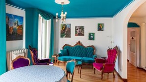 A room with a teal ceiling, a round table, a sofa, and chairs. There are paintings on the walls and a chandelier. - Appartamento Splendore (Bellagio)