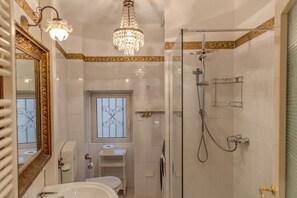 A bathroom with a shower, toilet, sink, and a chandelier. - Appartamento Splendore (Bellagio)