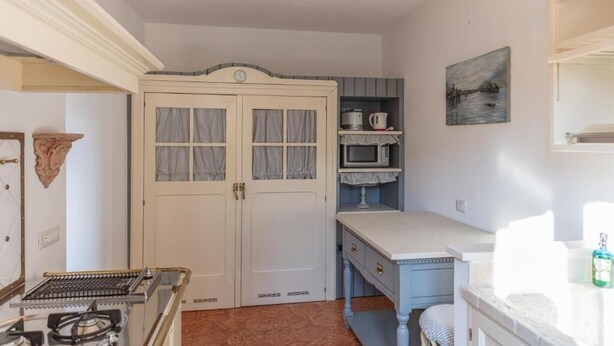 A room with a double door, a stove, a sink, a microwave, and a painting on the wall. - Appartamento Splendore (Bellagio)