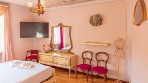 A bedroom with a bed, a dresser, a TV, a mirror, two chairs, a chandelier, and a mannequin. - Appartamento Splendore (Bellagio)