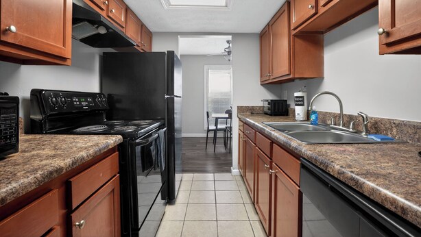 A kitchen with wooden cabinets, a black stove, a refrigerator, a sink, and a window with blinds. - Spacious 2BR with 1.5 baths, modern living (Riverdale)