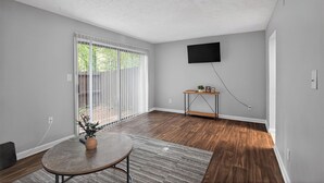 A room with a large sliding glass door, a flat-screen TV mounted on the wall, and a small wooden side table. - Spacious 2BR with 1.5 baths, modern living (Riverdale)