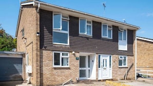 A two-story residential building with a brick facade, multiple windows, and a visible garage door. - House Sleeps 5 - Wifi & Tv (Luton)