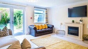 A living room with a sofa, a fireplace, a television, and a view of the outdoors. - House Sleeps 5 - Wifi & Tv (Luton)