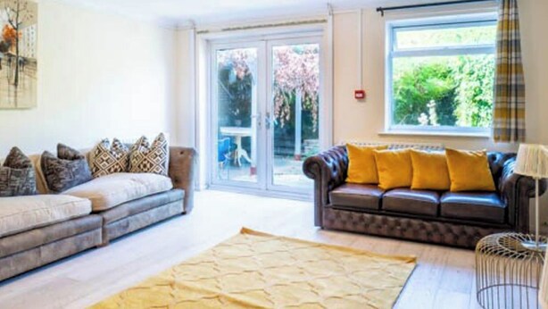 A living room with a sofa, a patterned rug, and a window with a view of greenery. - House Sleeps 5 - Wifi & Tv (Luton)