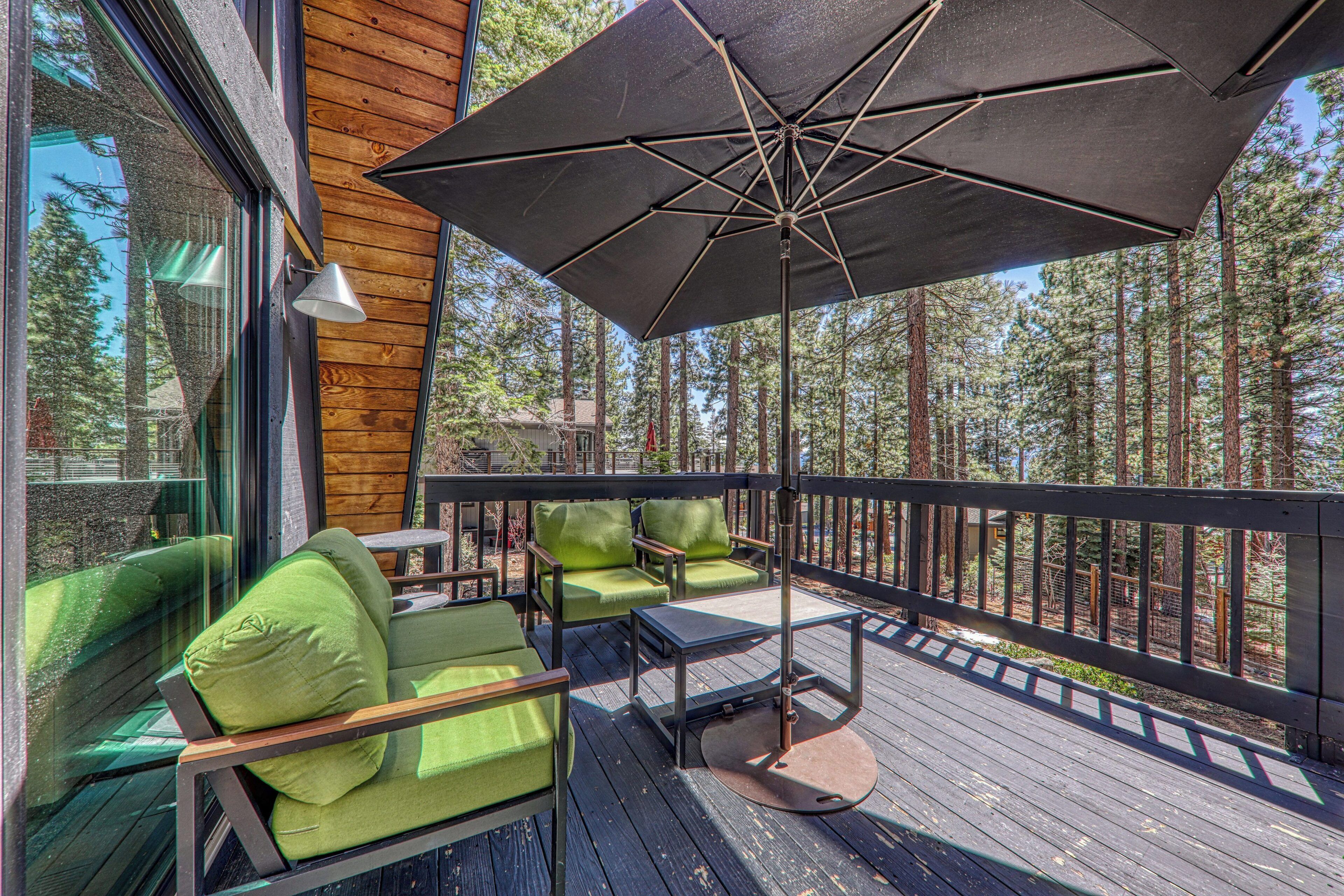 A wooden deck with green cushioned chairs, a table, and a large umbrella.