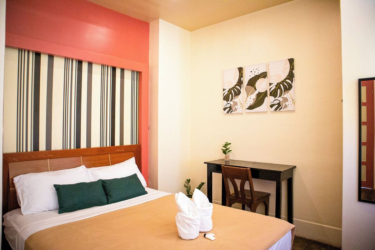 A hotel room with a bed, a desk, and two wall-mounted artworks.
