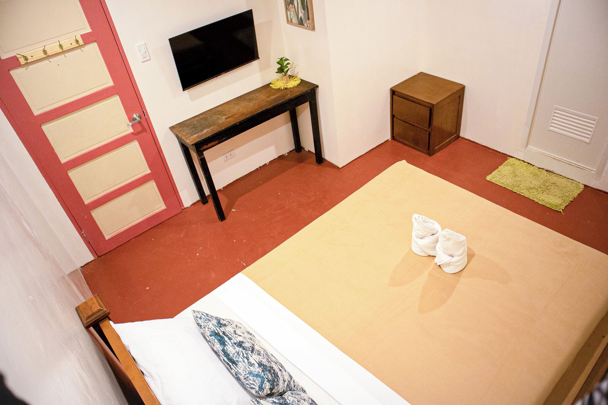 A room with a bed, a desk, a television, and a door with a red frame.