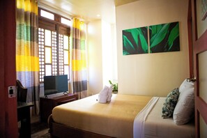 A hotel room with a bed, a TV, a desk, and a window with curtains.