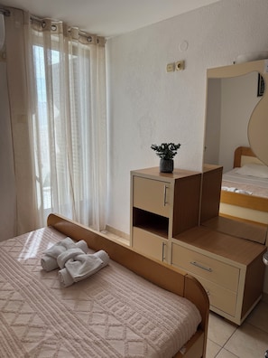 Een slaapkamer met een bed, een nachtkastje met een plant, een spiegel en een kledingkast.