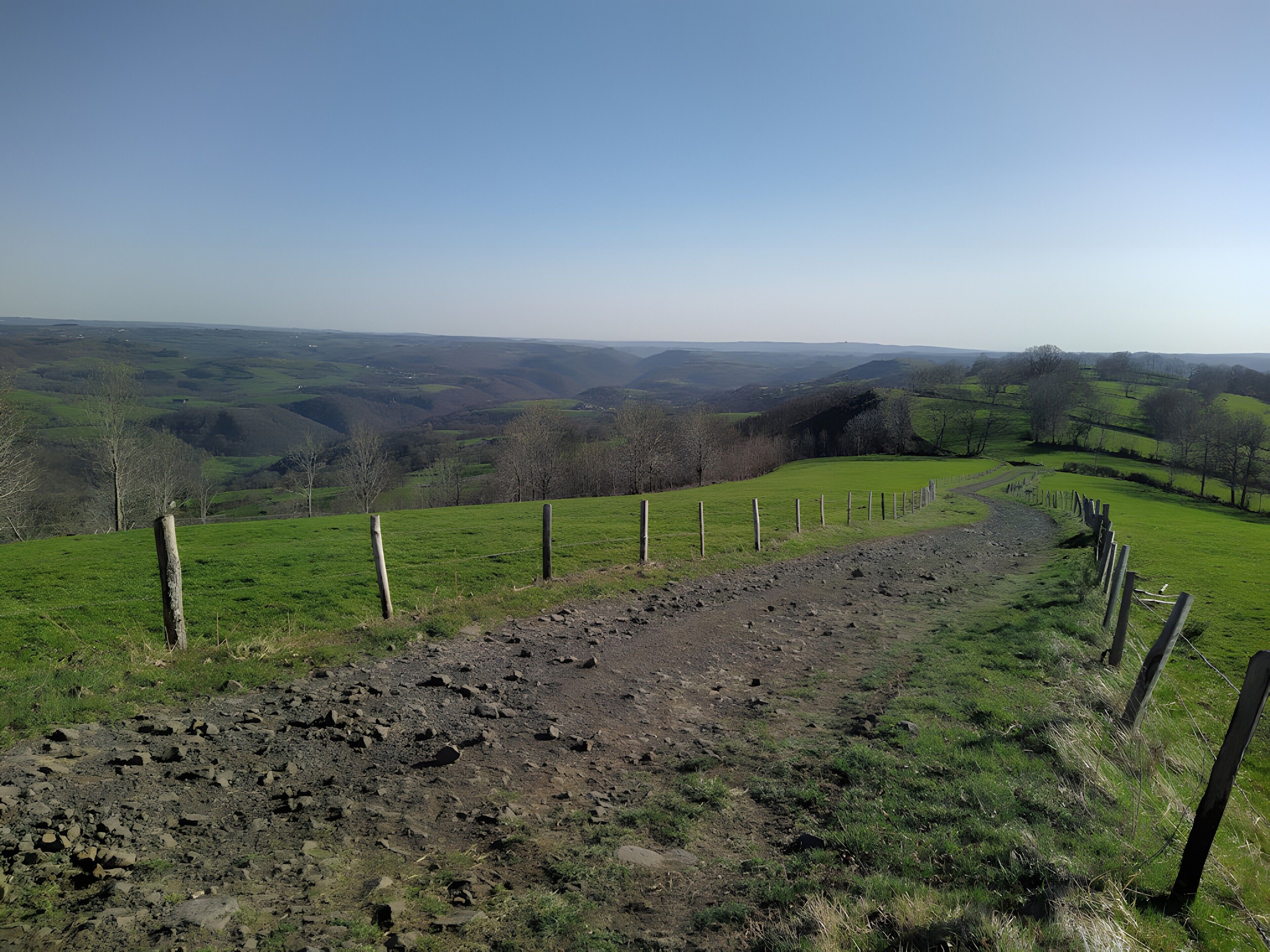 A rural landscape with a fenced path, rolling hills, and sparse trees.