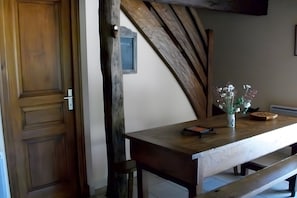 A wooden table with a vase of flowers, a framed picture on the wall, and a wooden bench.