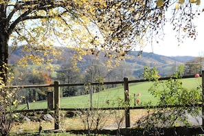 A rural landscape with a wooden fence, a stone wall, and a view of green fields and hills.