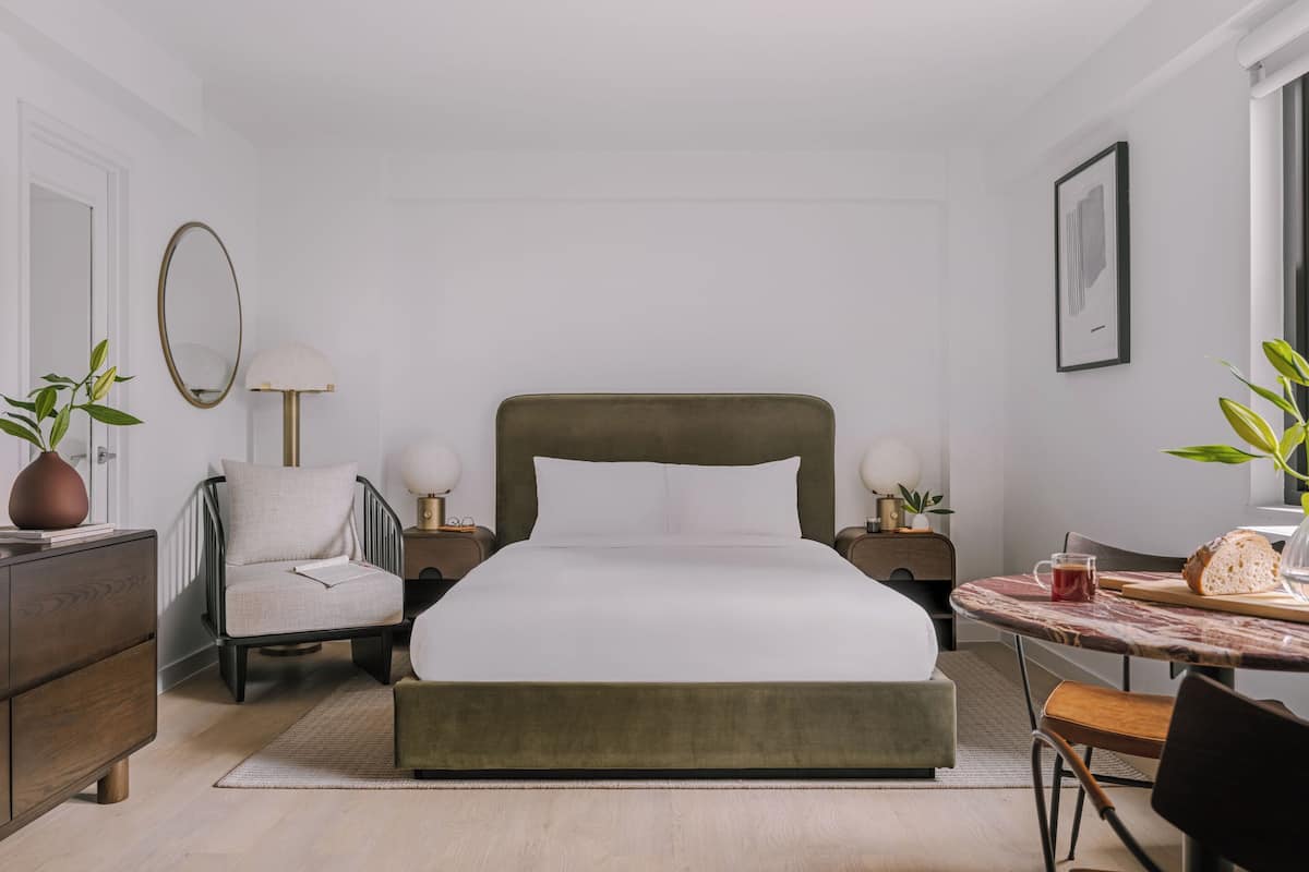 Quarto de hotel moderno com cama, uma cadeira, uma mesinha e uma escrivaninha.