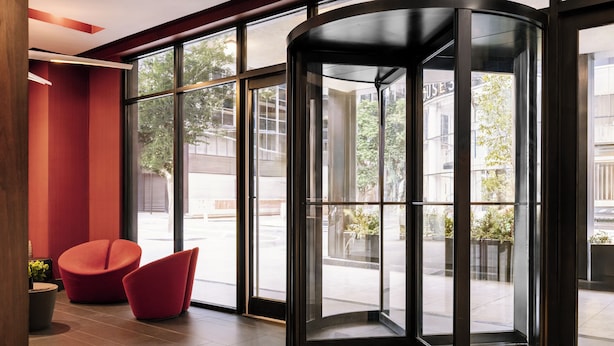 A modern lobby with a glass revolving door, red seating, and a view of the street outside. - Nester Finn Grand Central (New York)