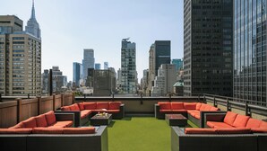 A rooftop terrace with outdoor seating, a view of a city skyline, and a green artificial turf area. - Nester Finn Grand Central (New York)