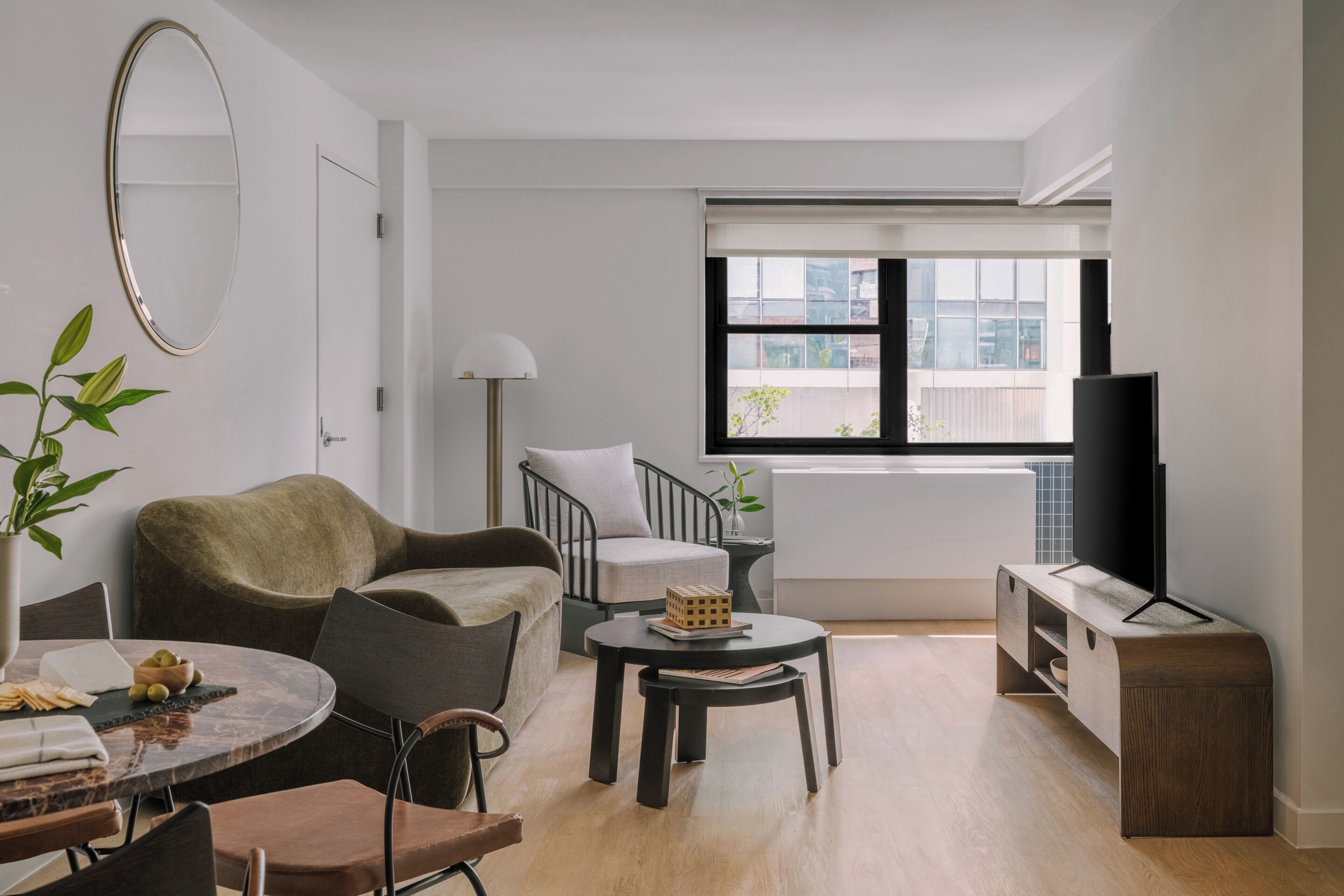 Una sala de estar moderna con un sofá, sillas, una mesa de centro, un televisor y un ventanal con vistas a edificios.