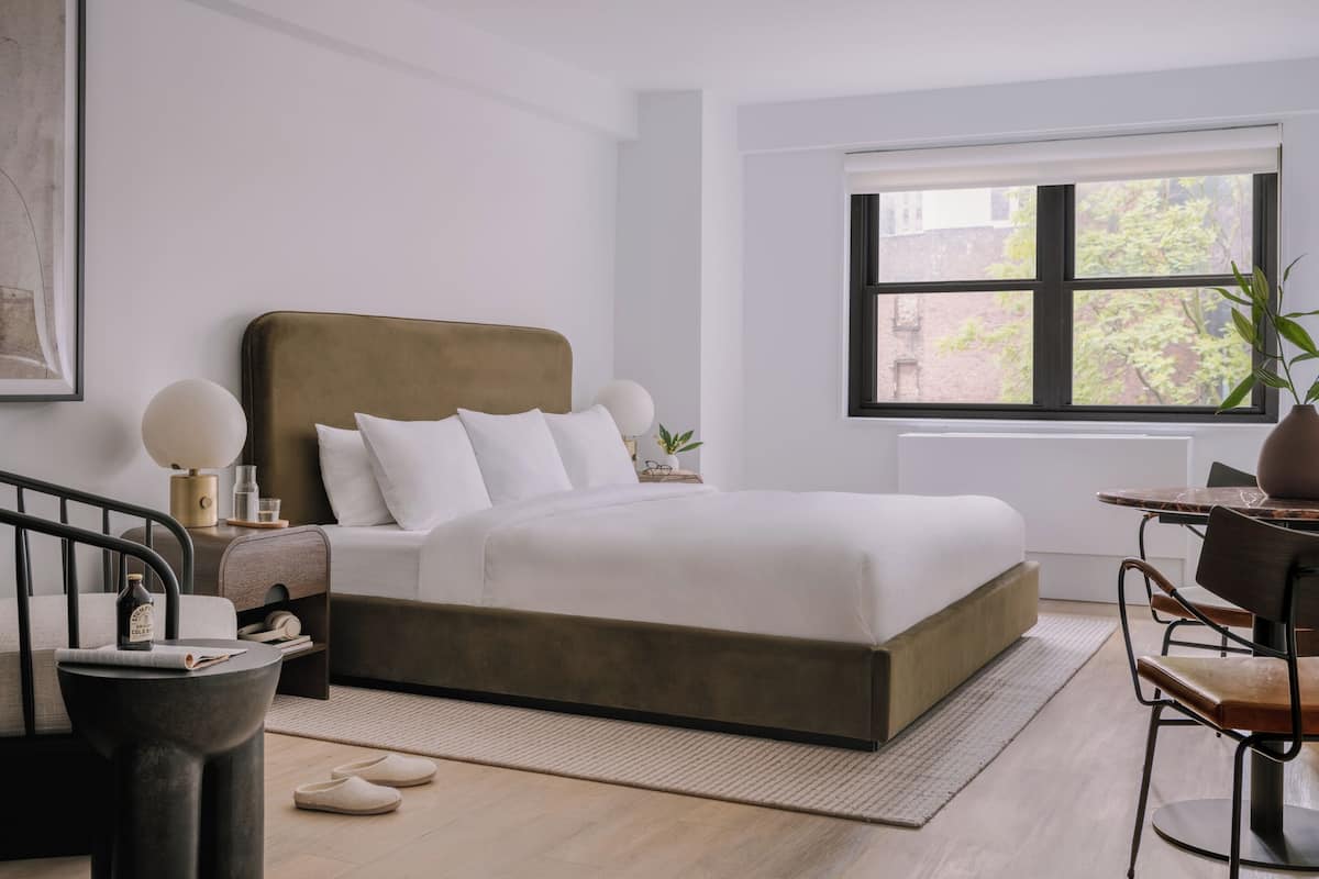 Quarto moderno com uma cama grande, mesas de cabeceira, uma cadeira, uma janela com vista e uma pequena mesa.