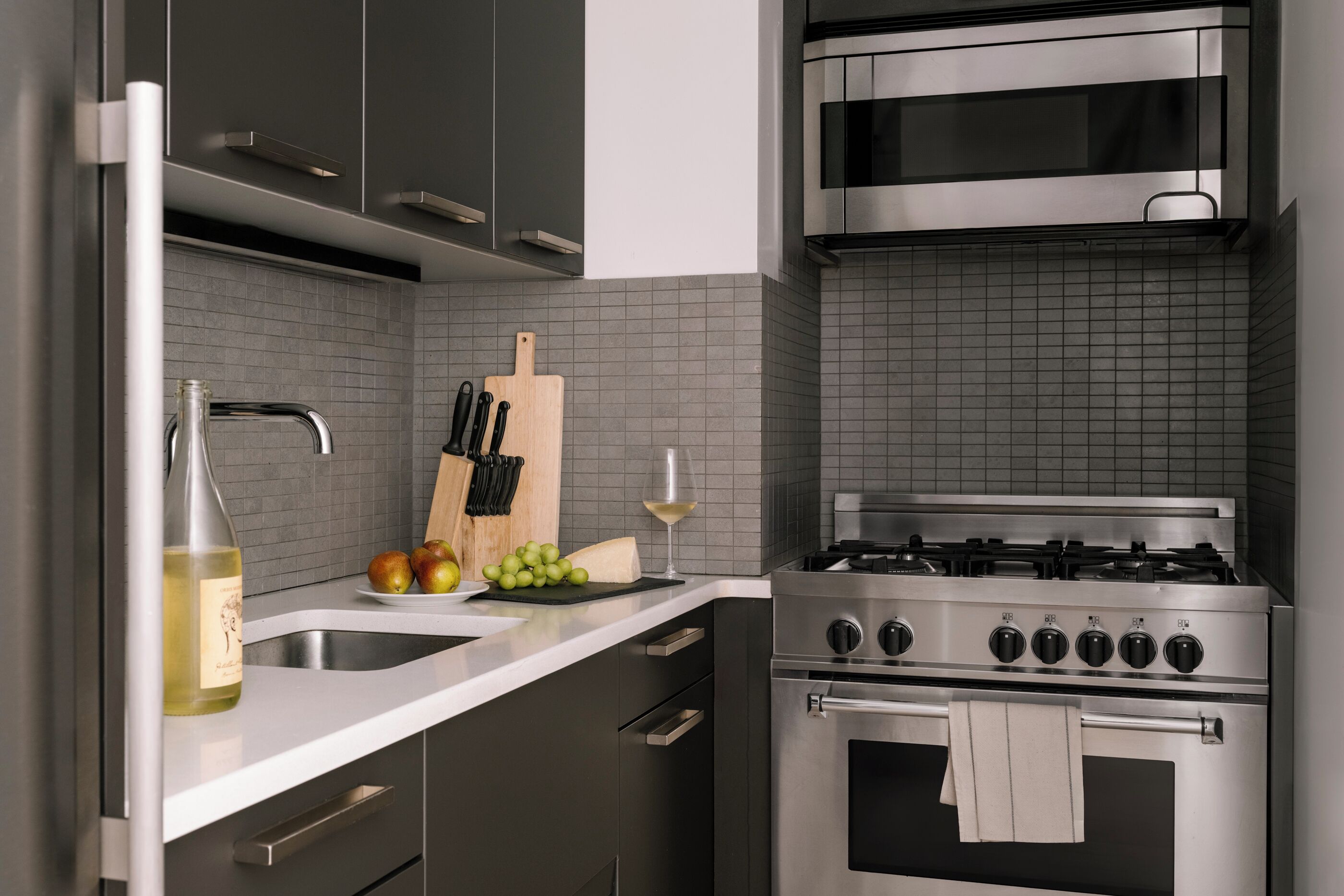 A modern kitchen with a stainless steel stove, a sink, and a countertop with a bottle and fruit.