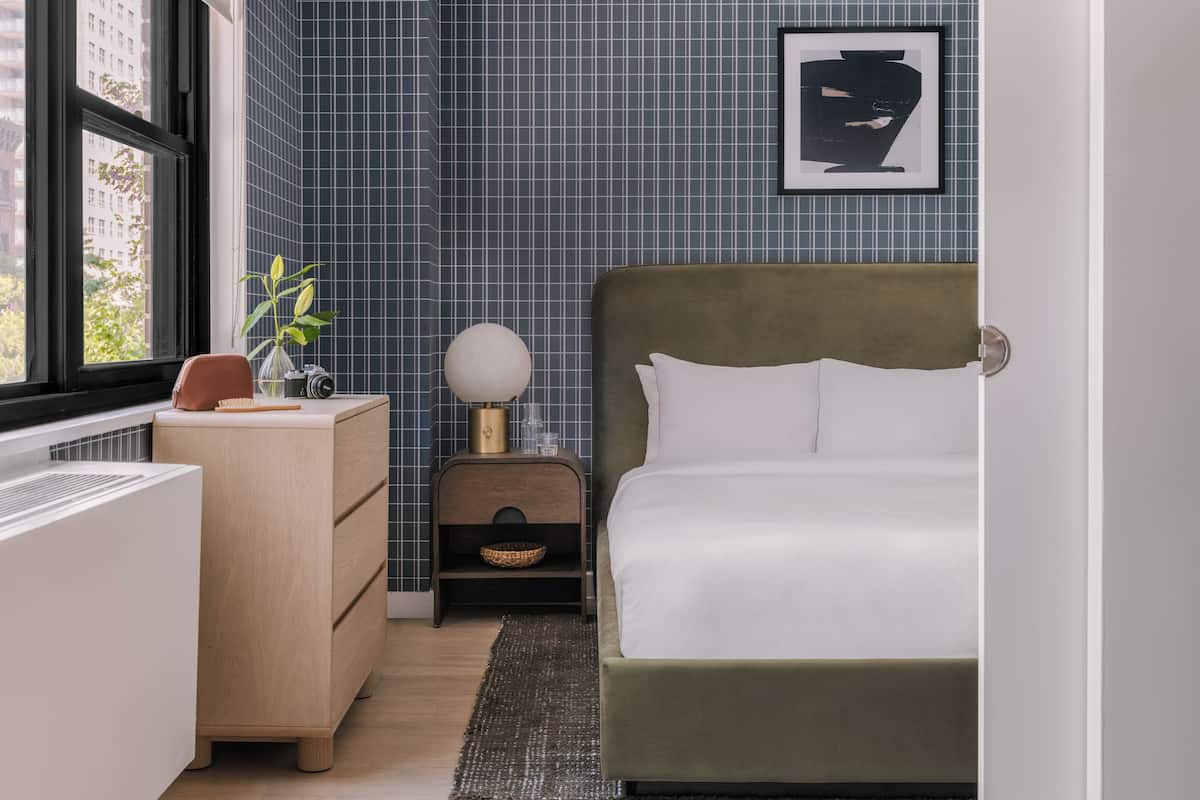 Quarto com cama, mesa de cabeceira, cômoda, janela e parede com padrão quadriculado.