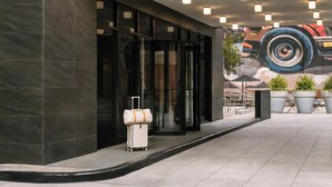 A modern building entrance with a glass door, a white suitcase, and outdoor seating. - Nester Finn Grand Central (New York)