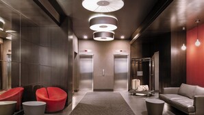 A modern elevator area with a red chair, a sofa, and a luggage cart. - Nester Finn Grand Central (New York)